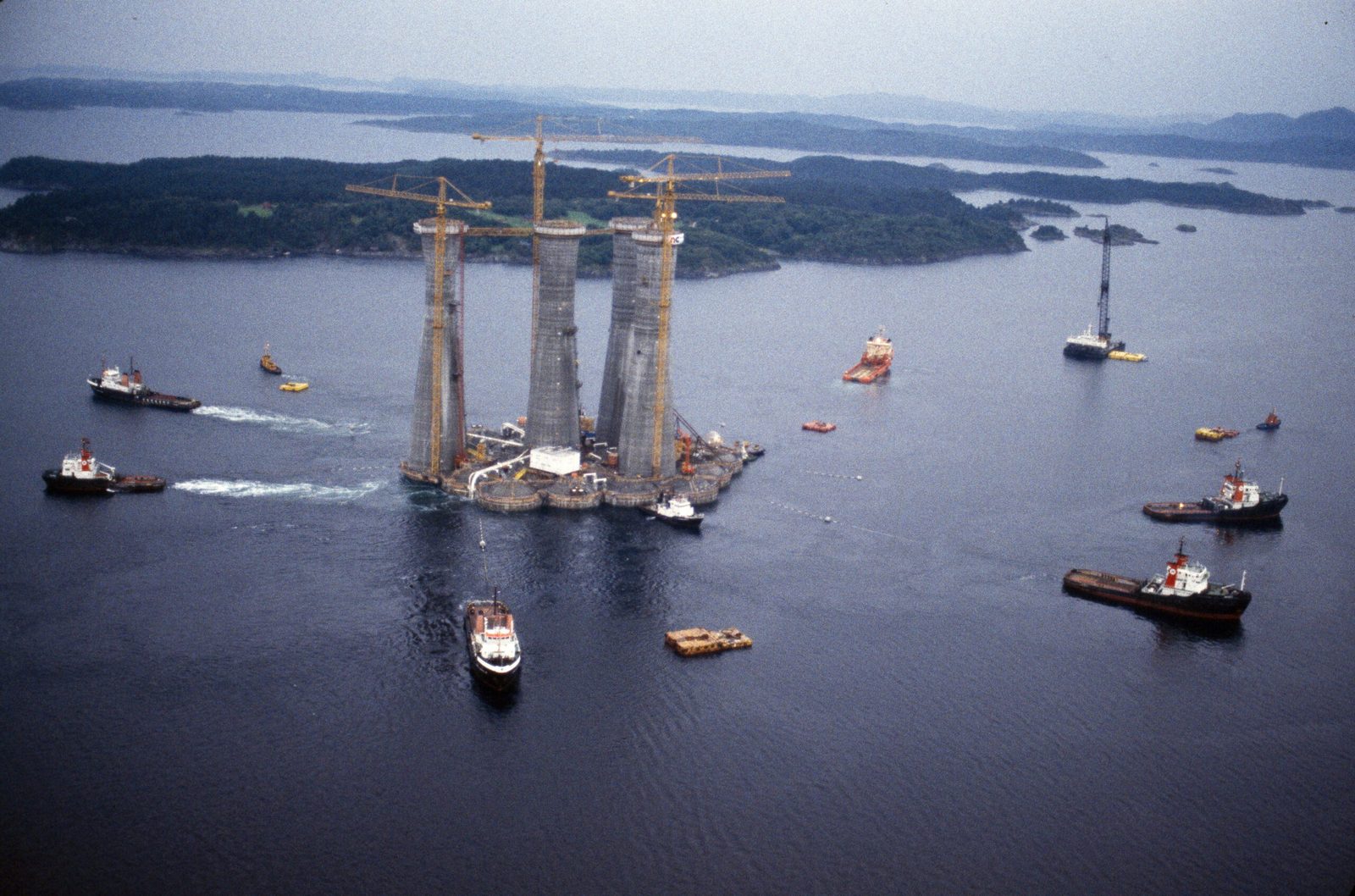 Gullfaks A's four concrete shafts under tow in Gandsfjorden with tower cranes and tugboats